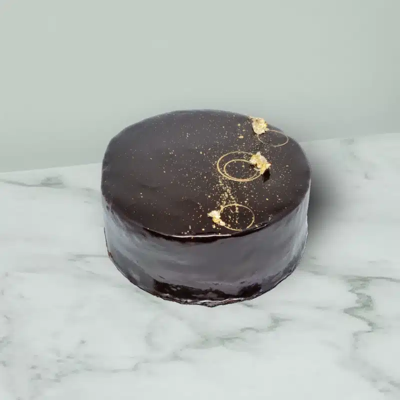 Chocolate cake with shiny mirror glaze topping and gold leaf decorations.